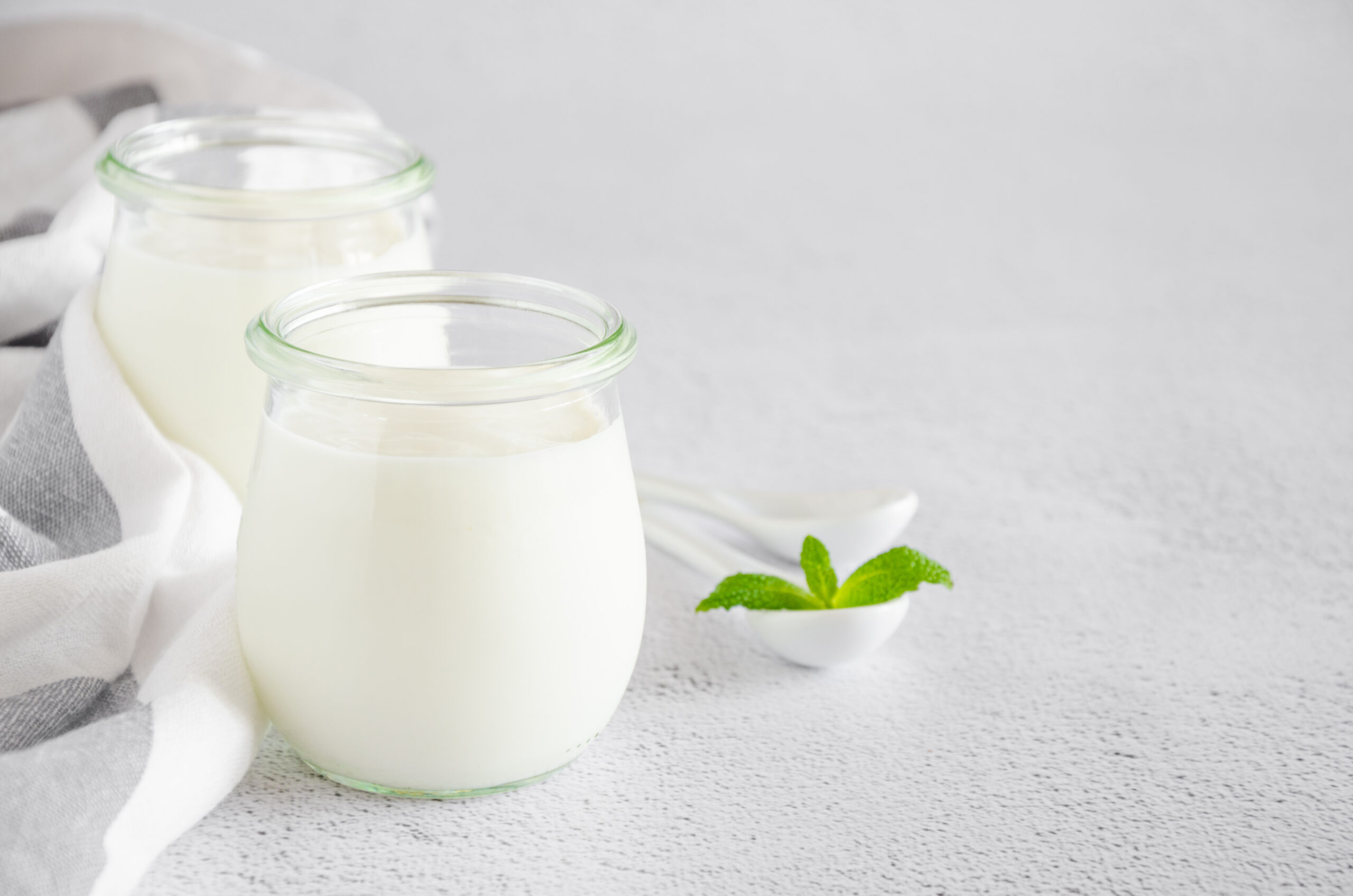 Homemade fresh organic yogurt in glass jars on a light background. Healthy food. Horizontal orientation. Copy space.
