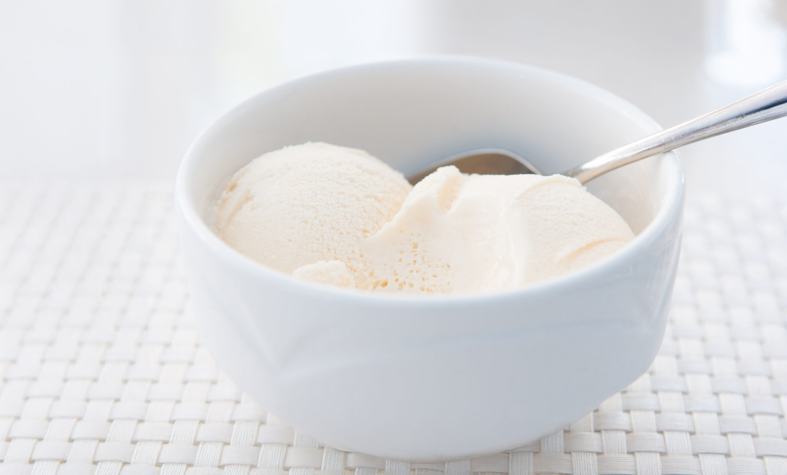 Closeup shot of white ice cream in a white bowl with a silver spoon