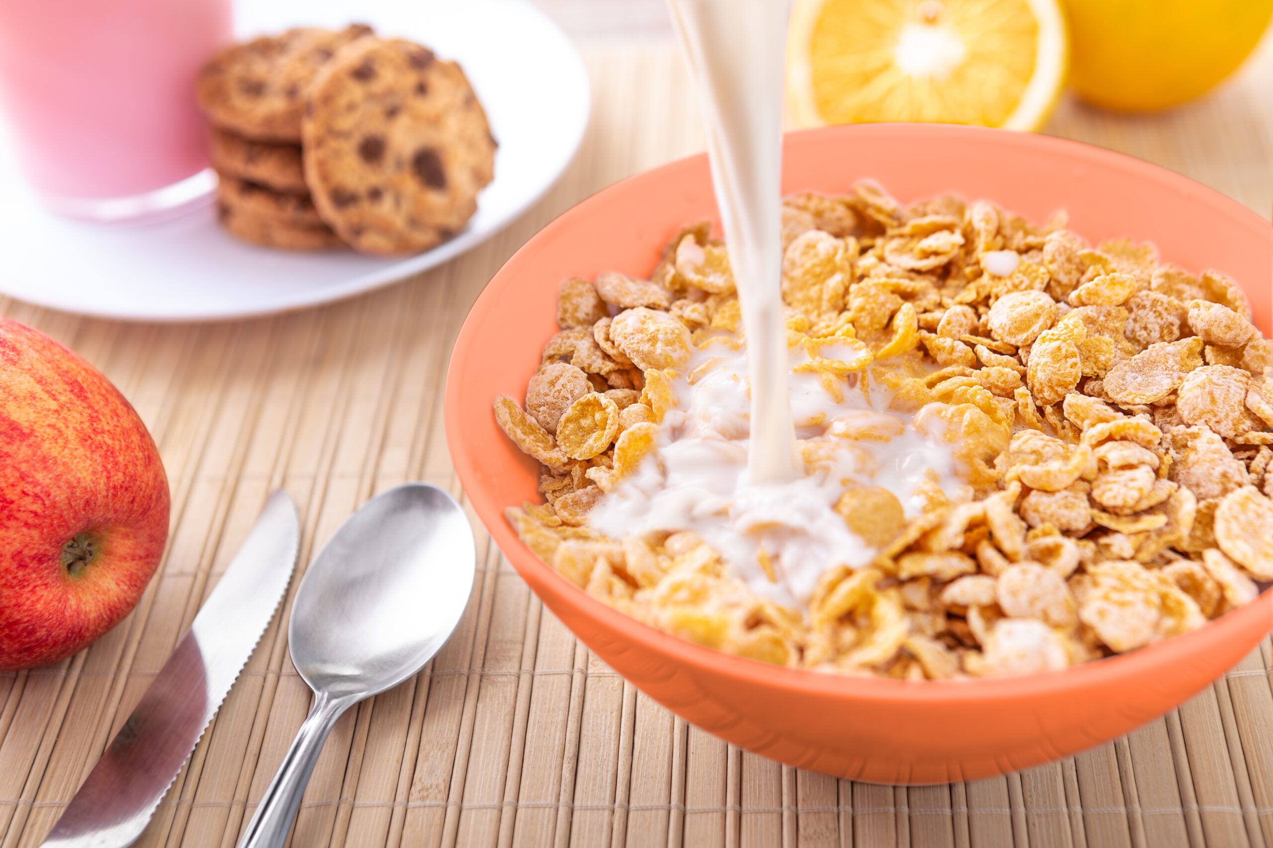 Breakfast pouring milk into corn flakes creating splash apple and orange fruit cookies