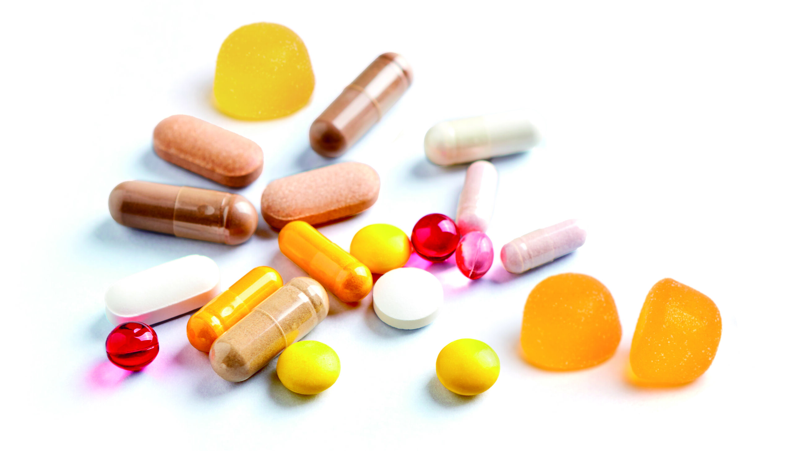 Multicolor vitamins and supplements on bright paper background. Concept for a healthy dietary supplementation. Copy space.